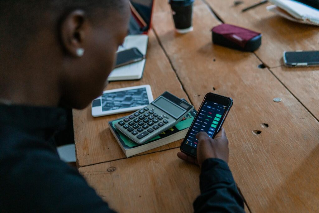 Fintech. Close-up of individual using smartphone for financial data analysis, calculator nearby on wooden table.
