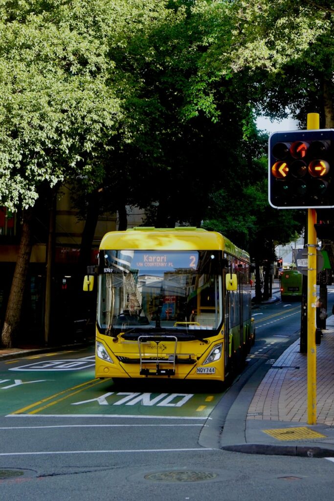 a yellow electric matatu driving down a street next to a traffic light